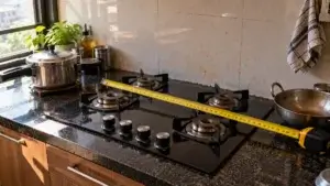 Steel tape measure laid across the width of a four burner gas hob in a kitchen